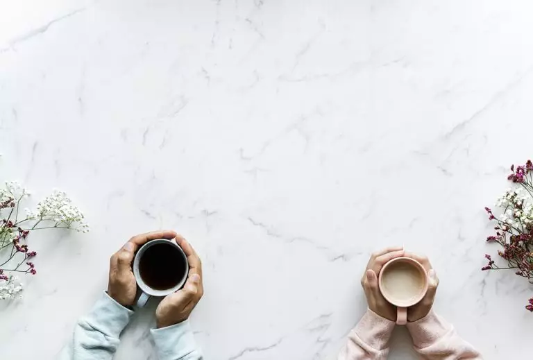 Image of two people holding warm drinks on a table